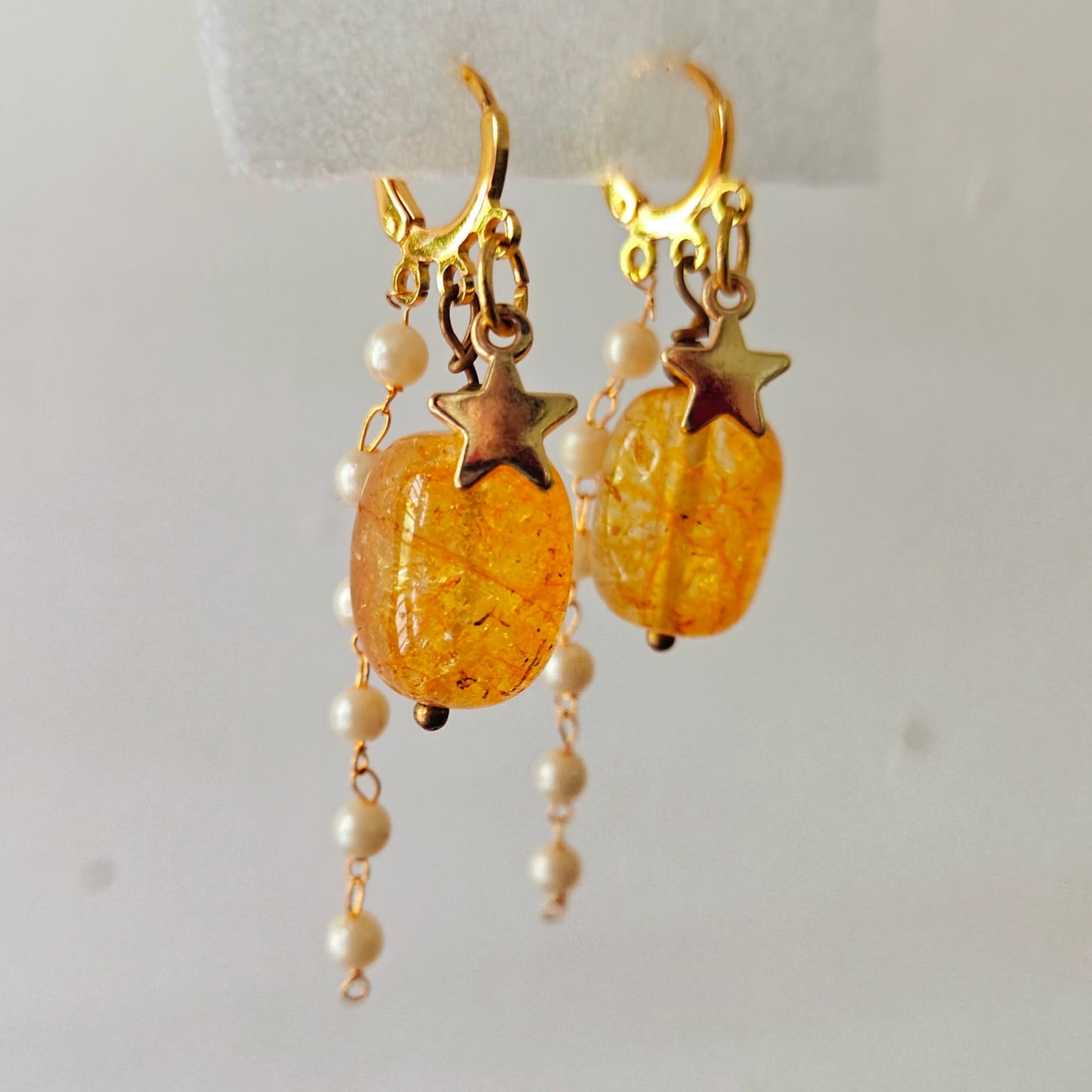 Gold earrings with amber beads and pearl-like elements on a white background