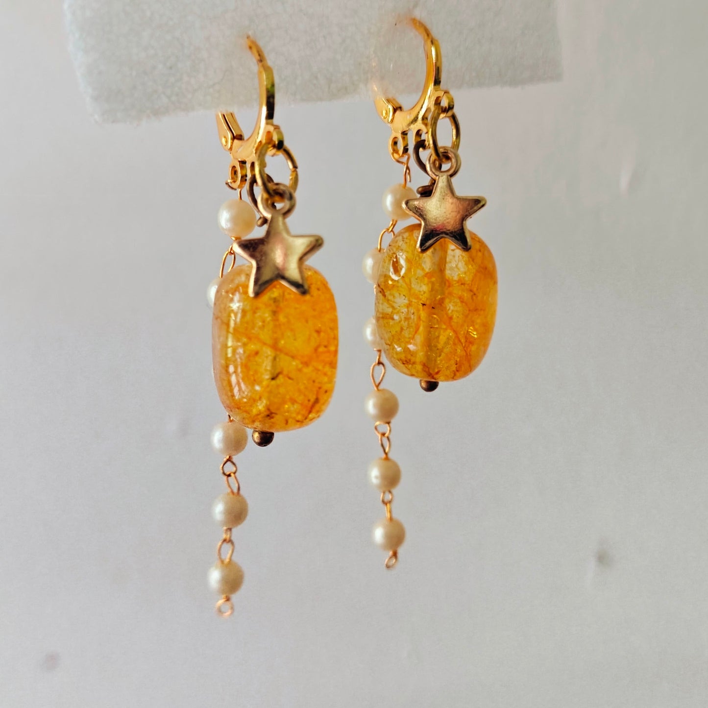 Gold earrings with star charms and amber-colored beads on a white background