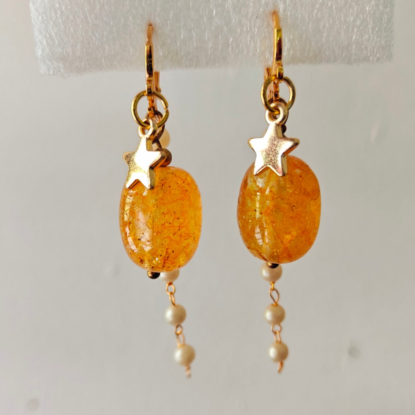 Pair of gold earrings with orange beads and star accents on a white background