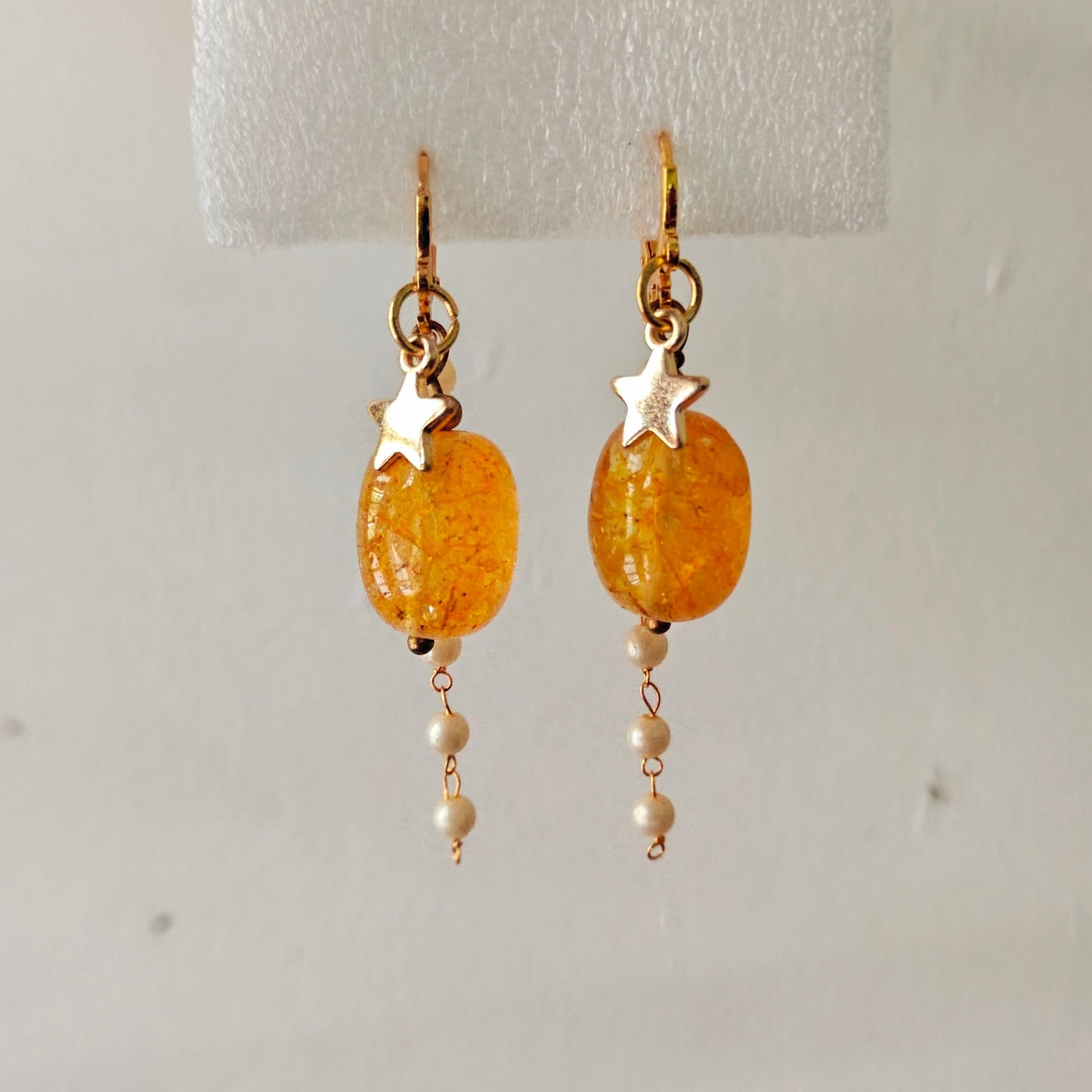Gold earrings with orange beads and star accents on a white background
