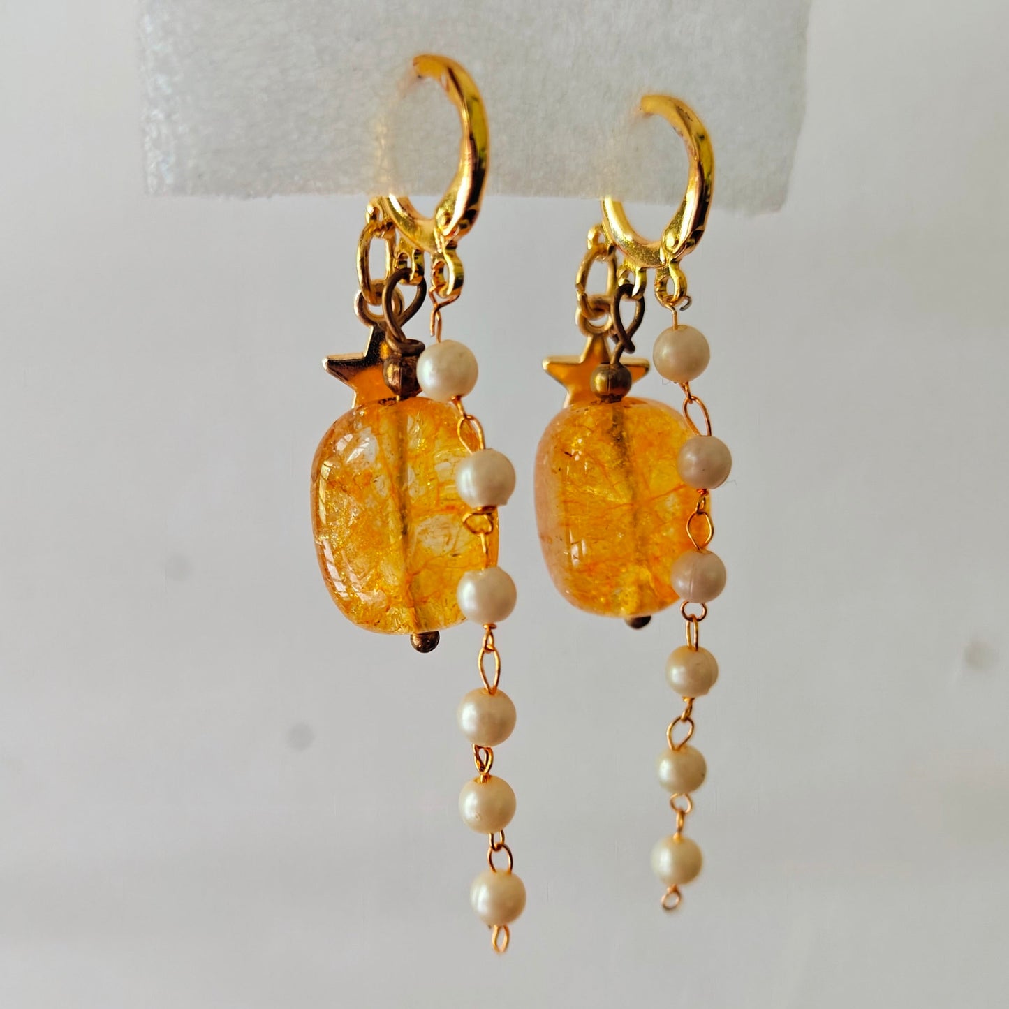 Gold earrings with amber beads and pearl-like strings on a white background