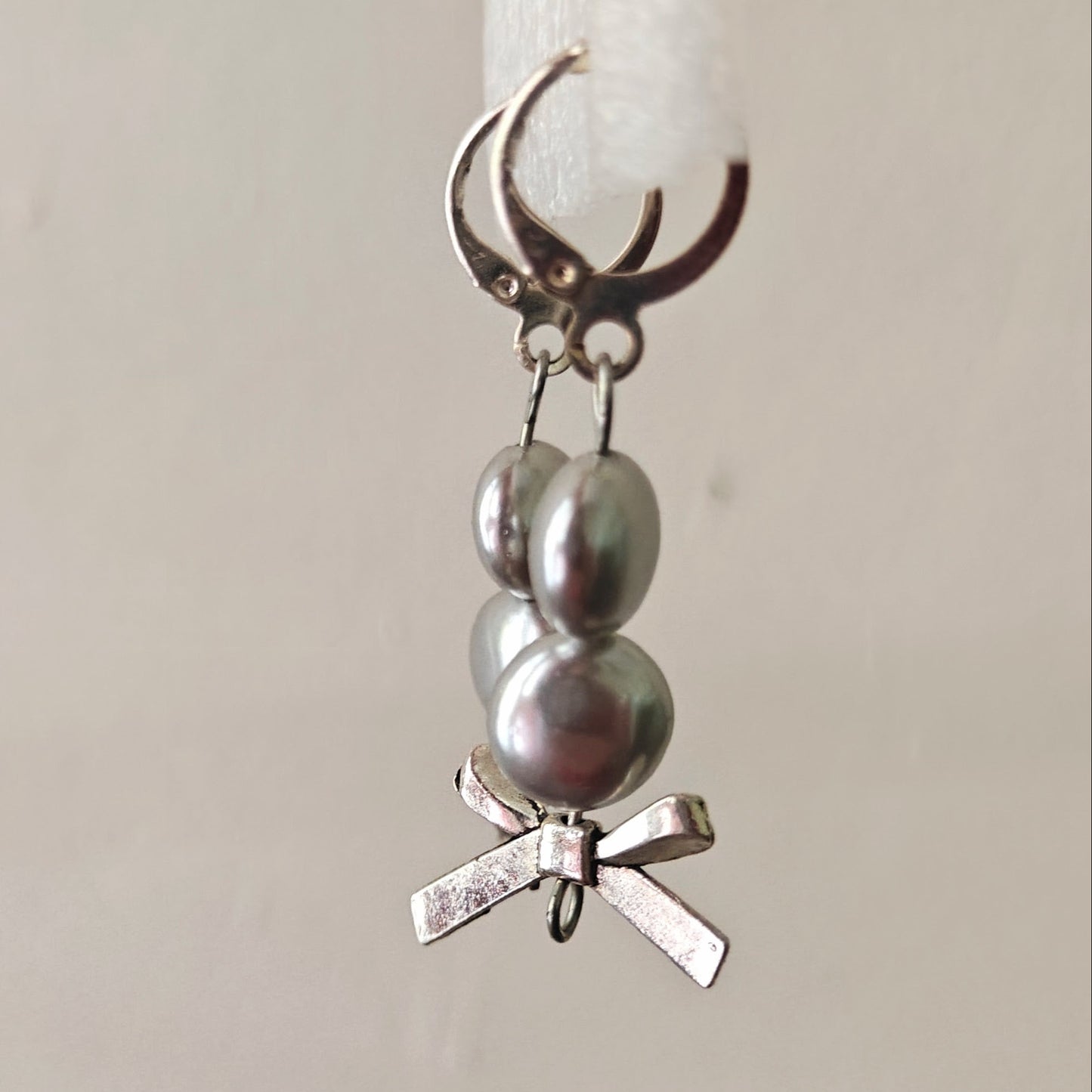 Silver charm with pearls and a bow on a white candle against a beige background