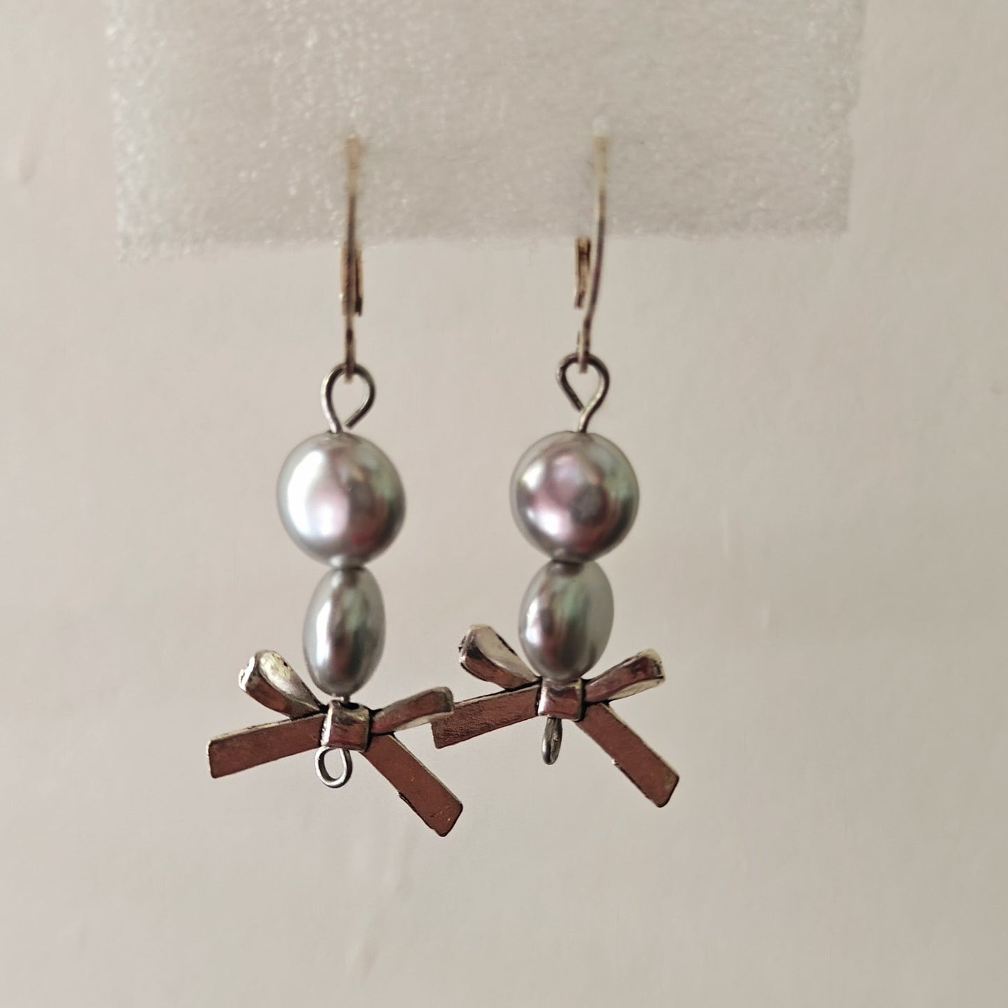 Pair of earrings with silver beads and bow accents on a white background