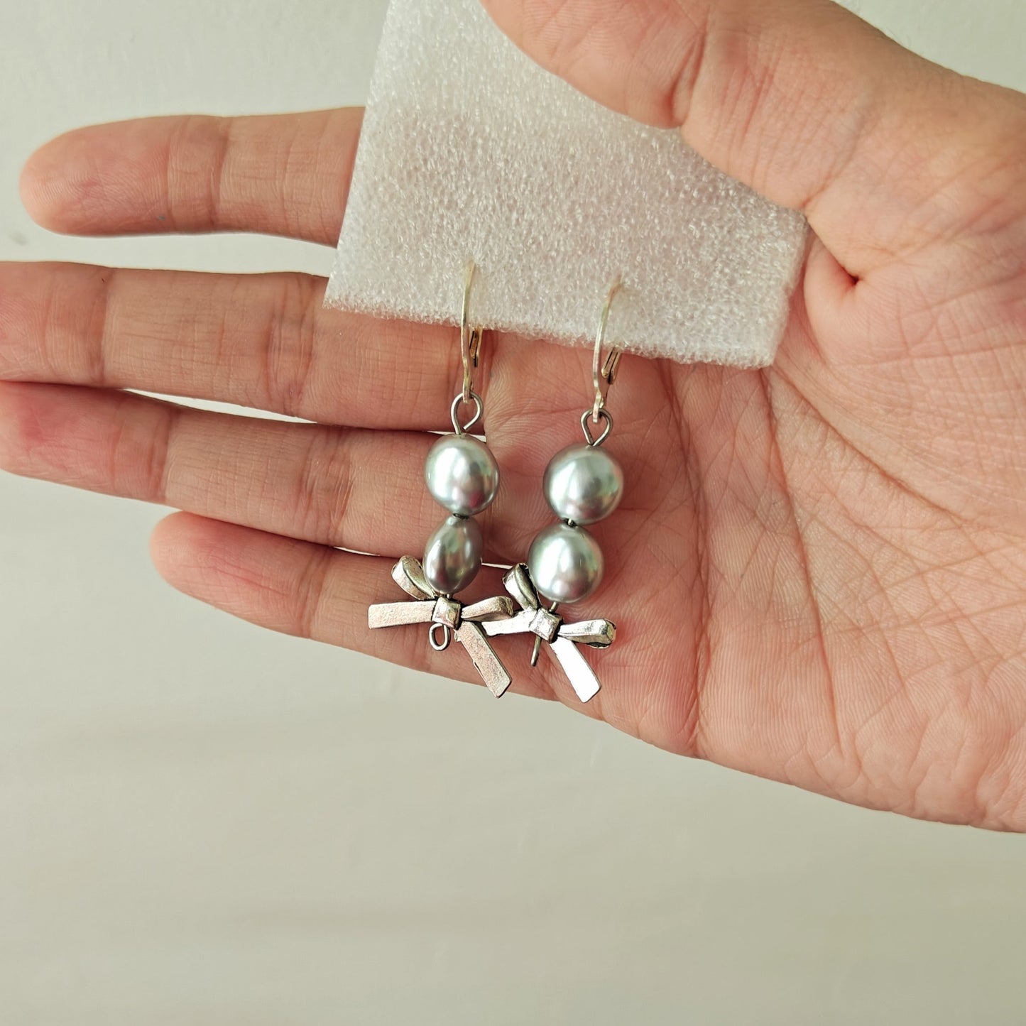 Hand holding a pair of silver earrings with a plain background