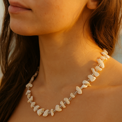 Close-up of a woman wearing a shell necklace with a blurred beach background