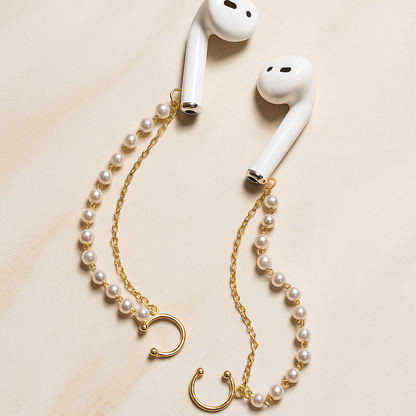 White AirPods with a pearl and gold chain accessory on a beige background