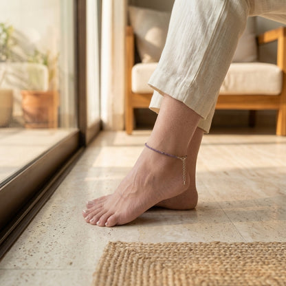 Person's foot with anklets on a stone floor in a home setting