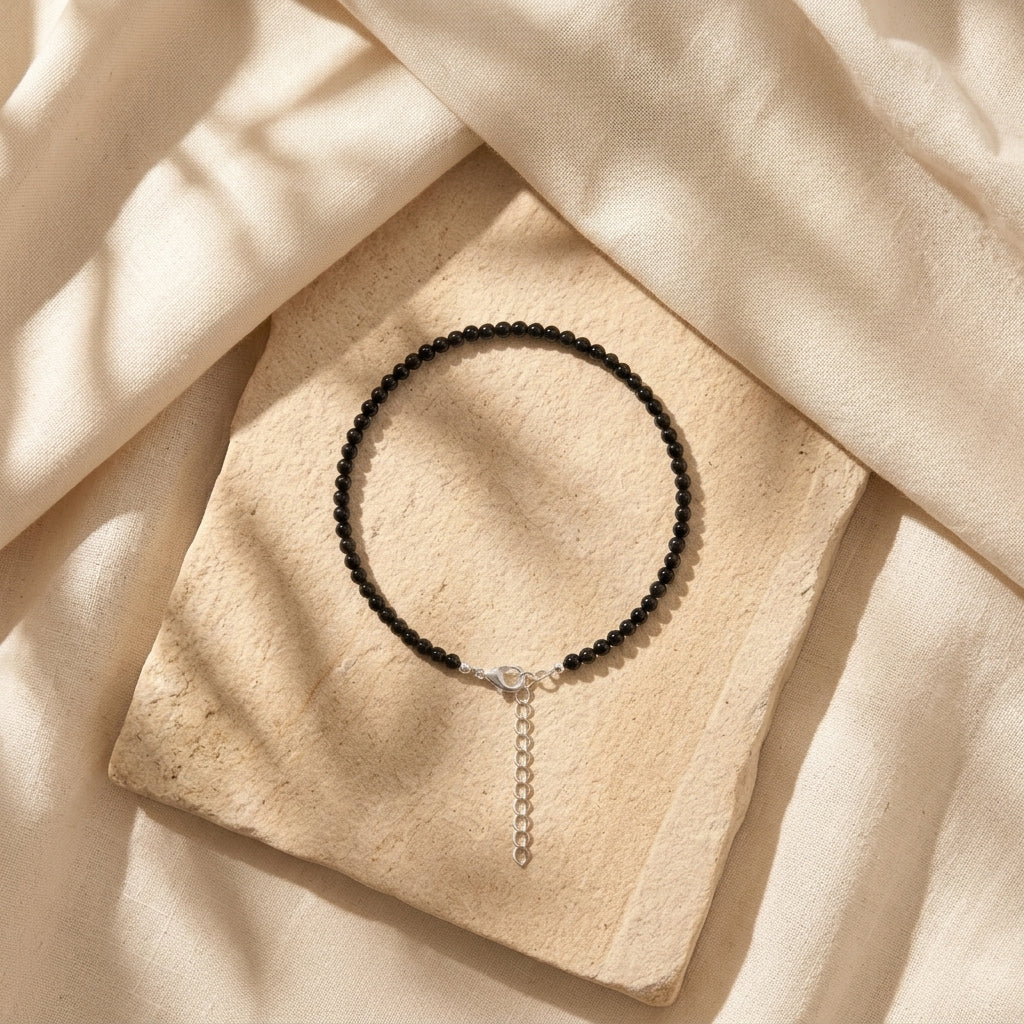Black beaded necklace with a silver chain on a beige stone surface