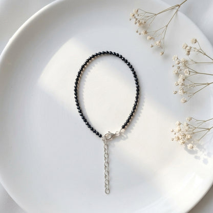 Black beaded necklace on a white plate with dried flowers
