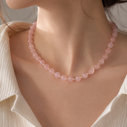 A close-up of a woman wearing a delicate pink beaded necklace with small gold spacer beads, paired with a cream-colored top.
