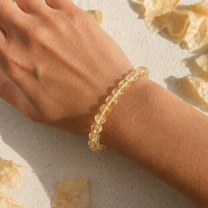 Hand wearing a gold citrine beaded bracelet on a light background with dried flowers.