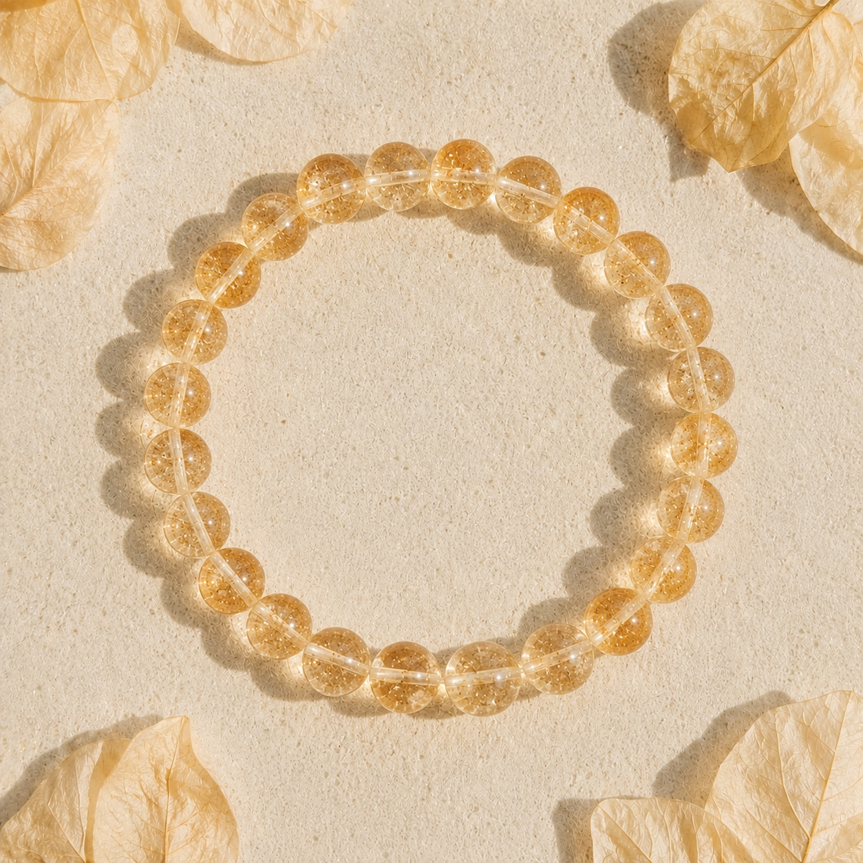 Gold citrine beaded bracelet on a beige background with dried leaves