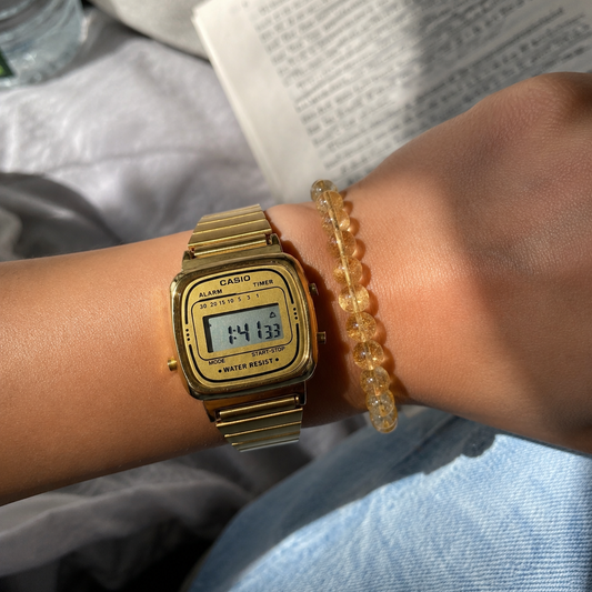 Gold digital watch and citrine bracelet on a wrist with a blurred background