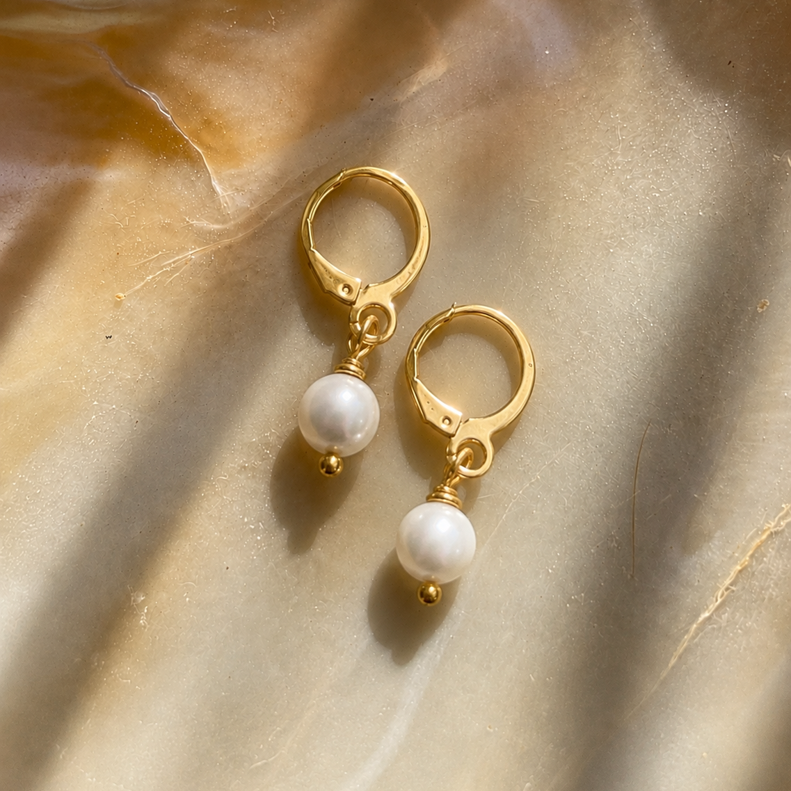 Gold hoop earrings with pearl drops on a beige fabric background