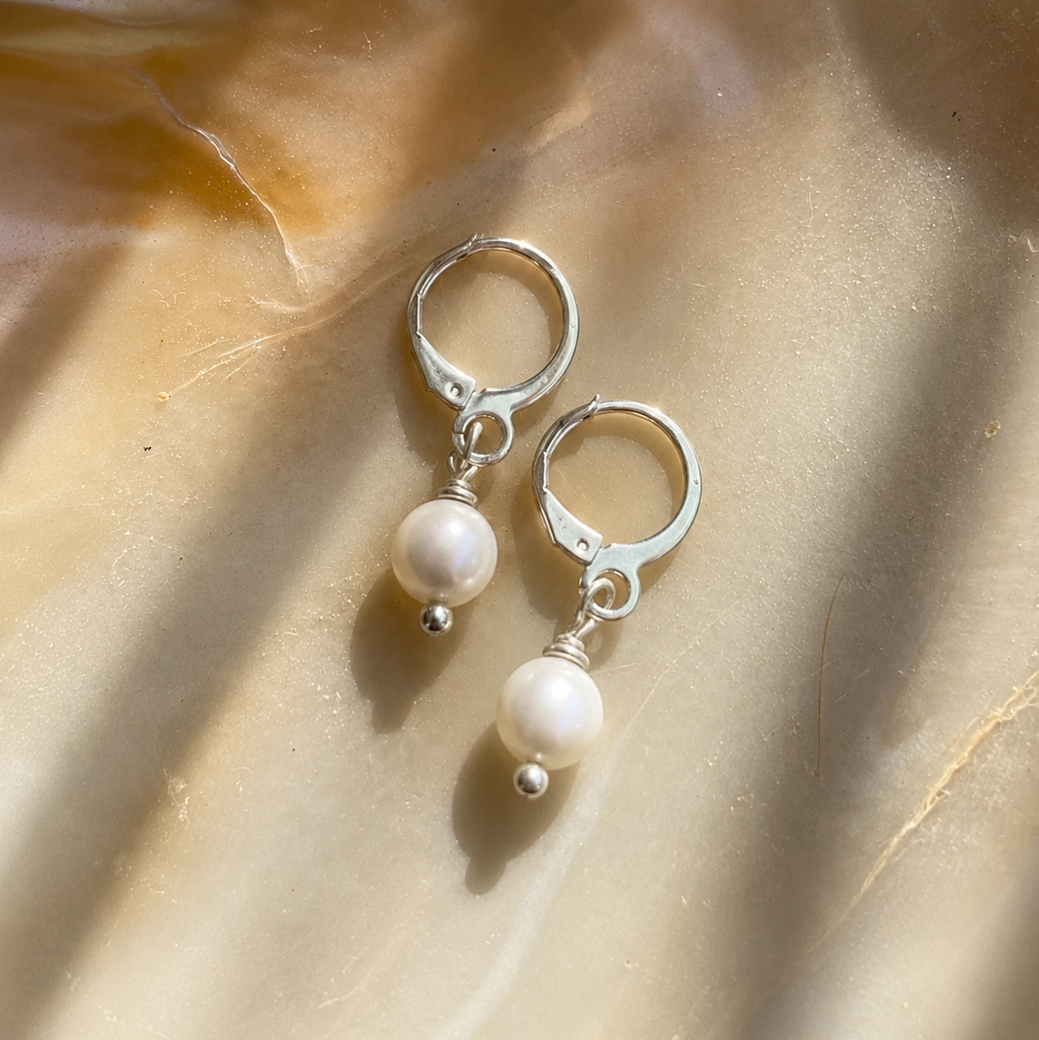 Silver earrings with pearl drops on a beige fabric background