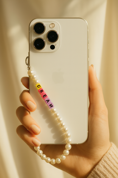 Phone case with a pearl strap and colorful letters held by a hand against a neutral background