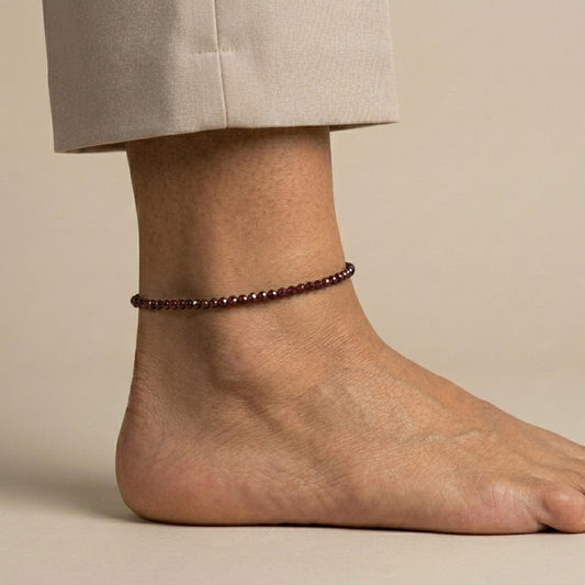 Ankle with a red beaded anklet on a neutral background