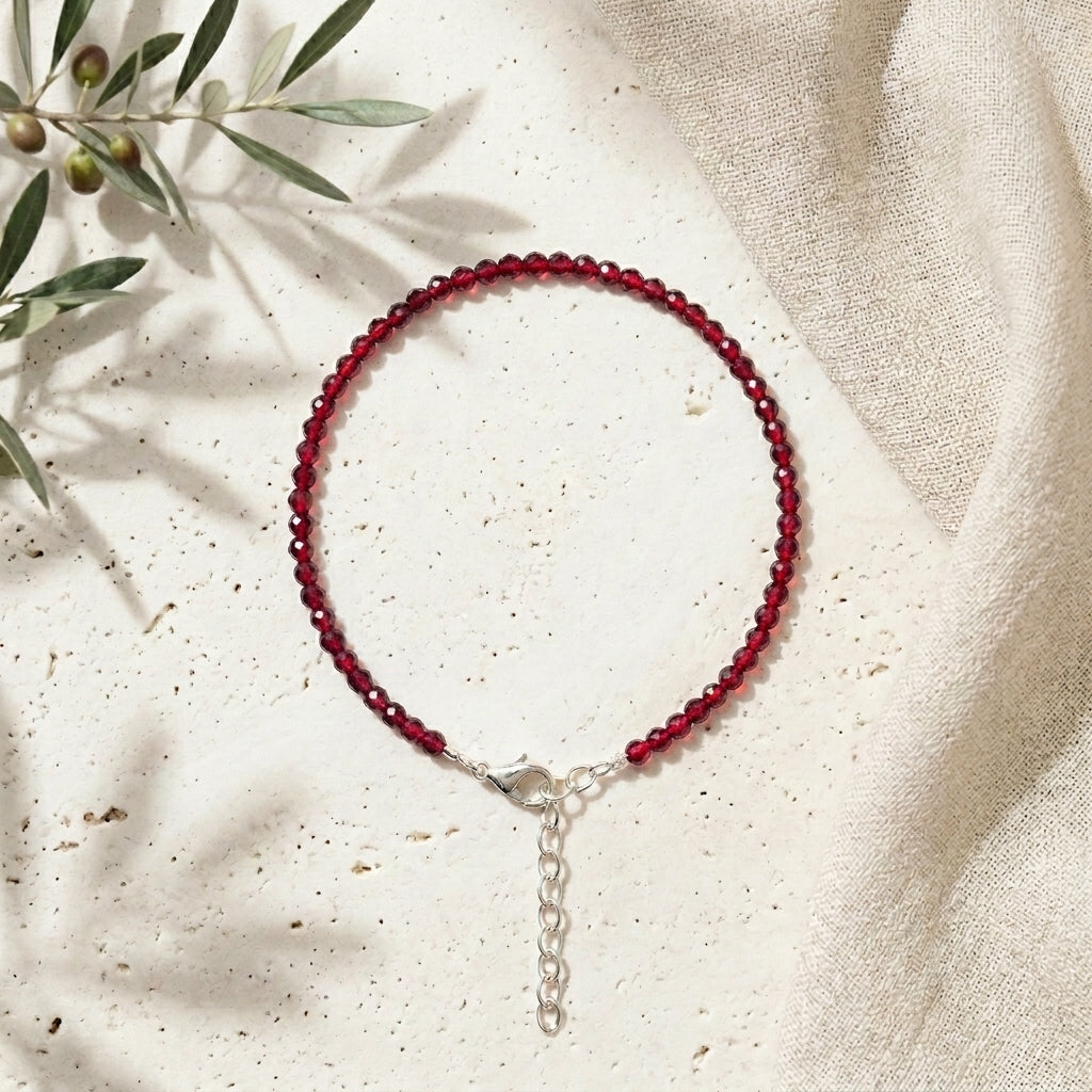 Red beaded bracelet on a beige fabric background with green leaves.