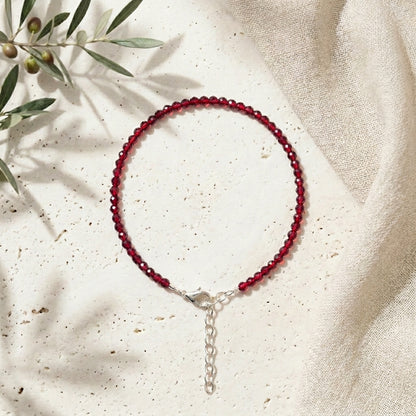 Red beaded bracelet on a beige fabric background with green leaves.