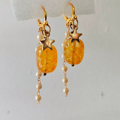Gold earrings with star charms and amber-colored beads on a white background
