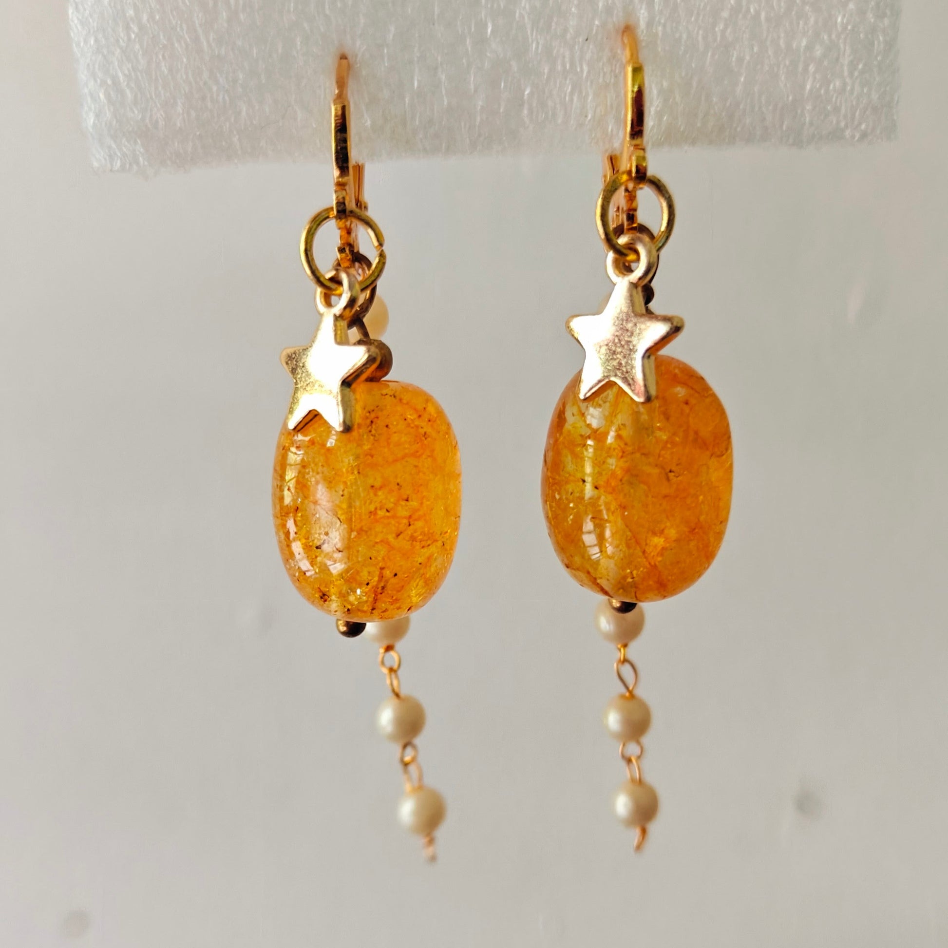 Pair of gold earrings with orange beads and star accents on a white background