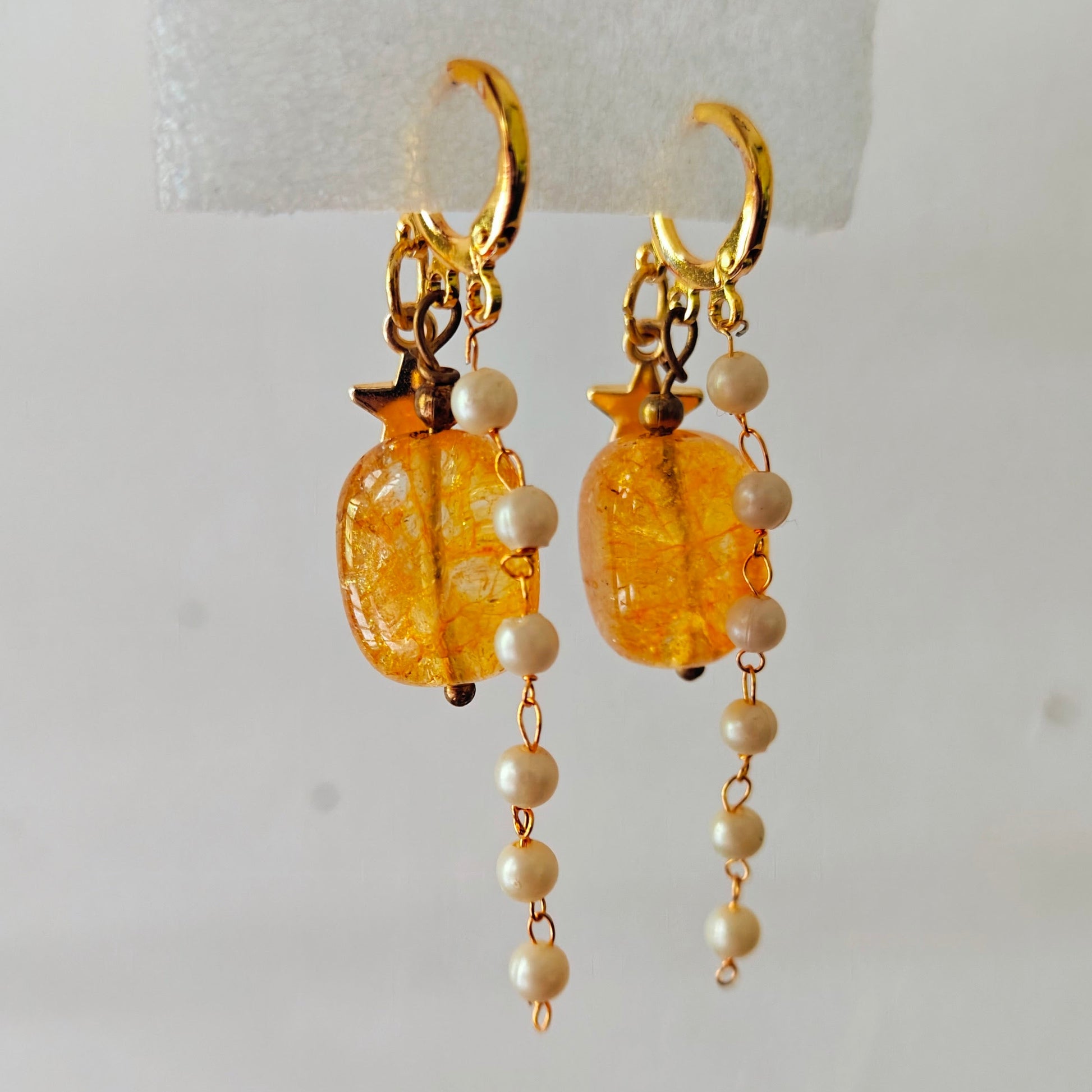 Gold earrings with amber beads and pearl-like strings on a white background
