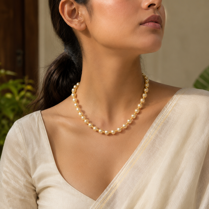 A woman wearing a classic strand of cream-colored freshwater pearl necklace with a matching pearl hair pin, dressed in a light beige sari.