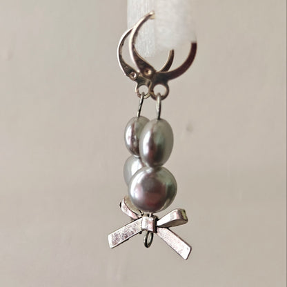 Silver charm with pearls and a bow on a white candle against a beige background