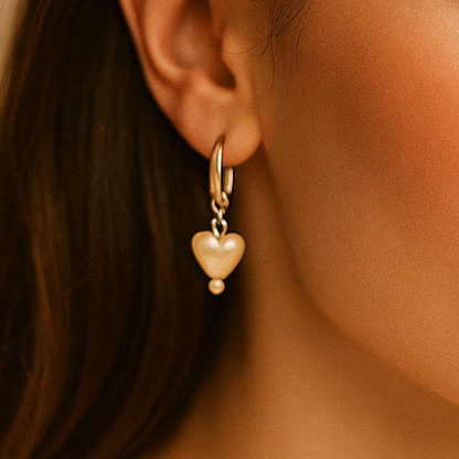 Close-up of a woman wearing gold heart-shaped earrings against a beige background