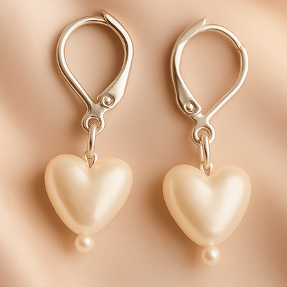 Heart-shaped pearl earrings with gold hooks on a beige background