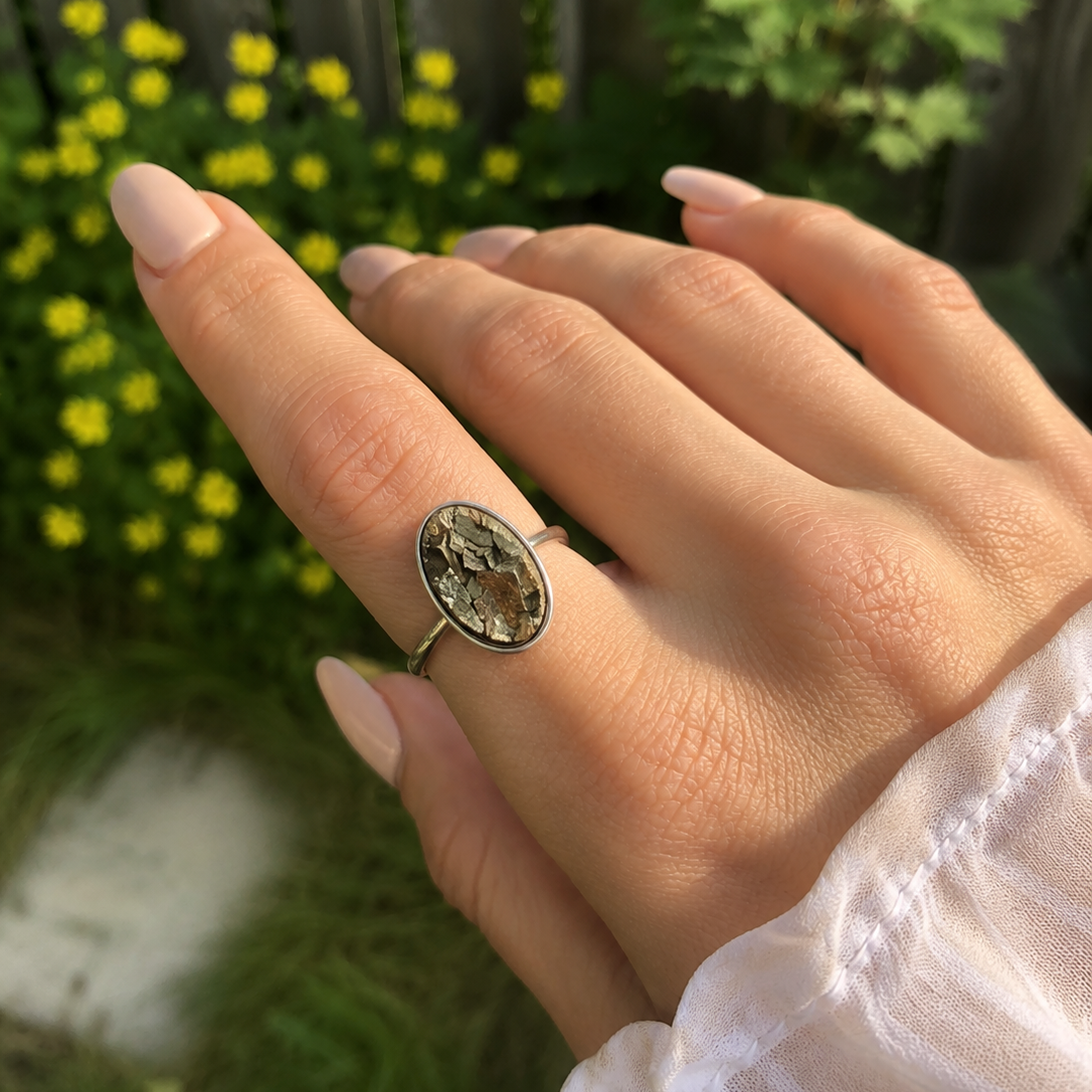 Hand wearing a decorative pyrite ring with a blurred natural background