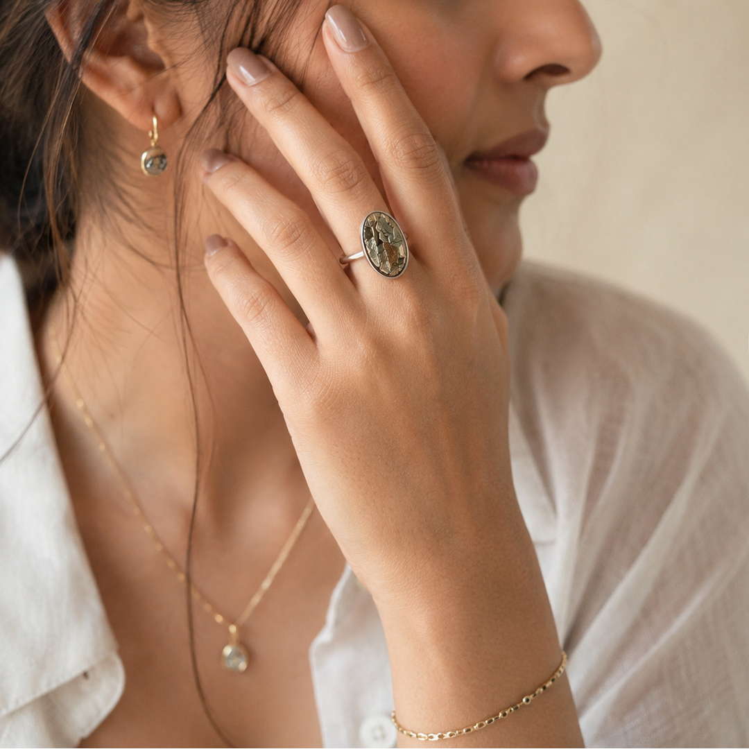 Woman wearing gold jewelry including earrings, pyrite ring, and necklace against a neutral background