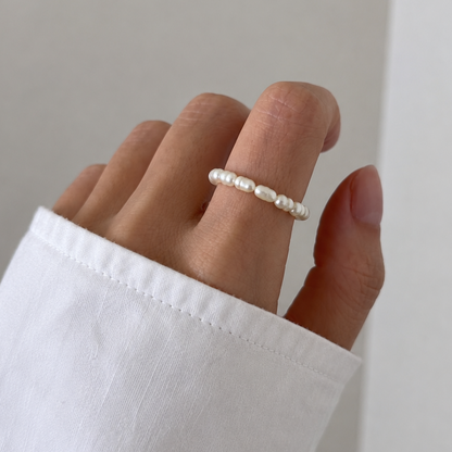 Hand wearing a pearl ring on a plain background
