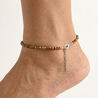 Ankle bracelet with brown beads and a chain on a light background
